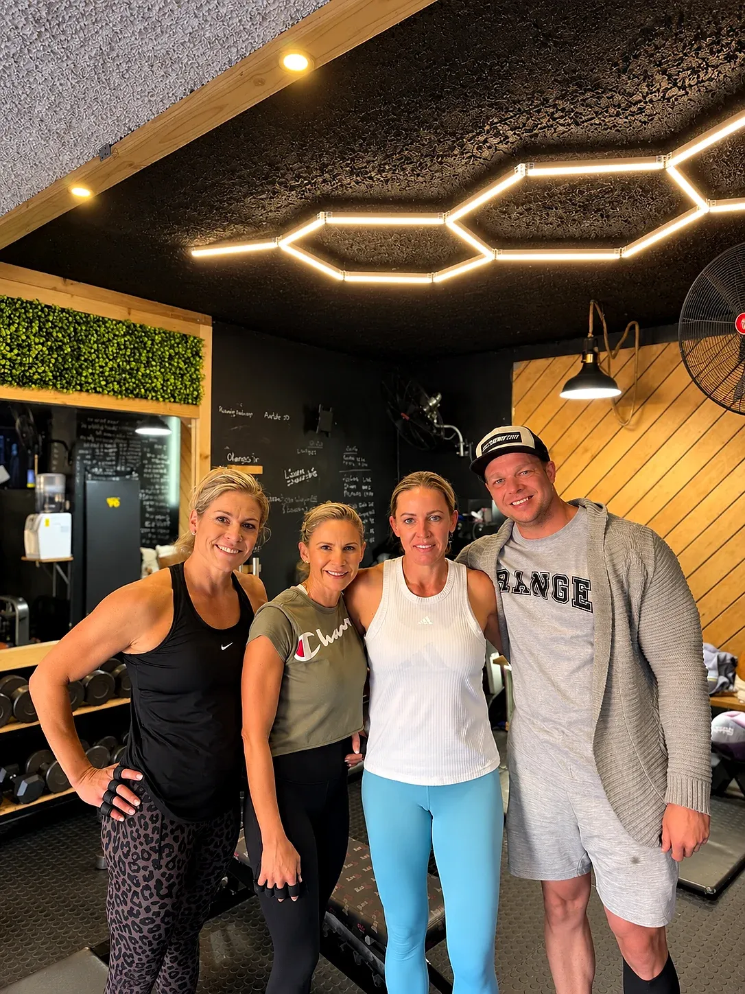 People smiling inside the XO Fit gym, under the hexagon lights